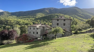 A stone building with a tiled roof, surrounded by lush greenery and hills in the background.