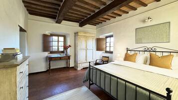 A bedroom with a wooden ceiling, a bed with a metal frame, a radiator, a window, and a chair.