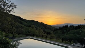 A rectangular pool with a wooden deck and stone edging, surrounded by a metal fence. - Bio Agriturismo il Vigno (Caprese Michelangelo)