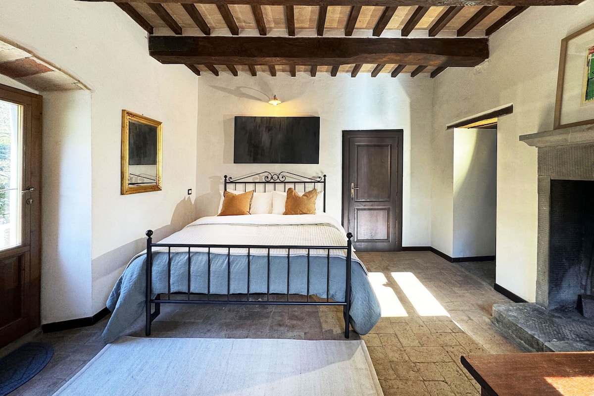 A bedroom with a bed, wooden beams, a fireplace, and a door.