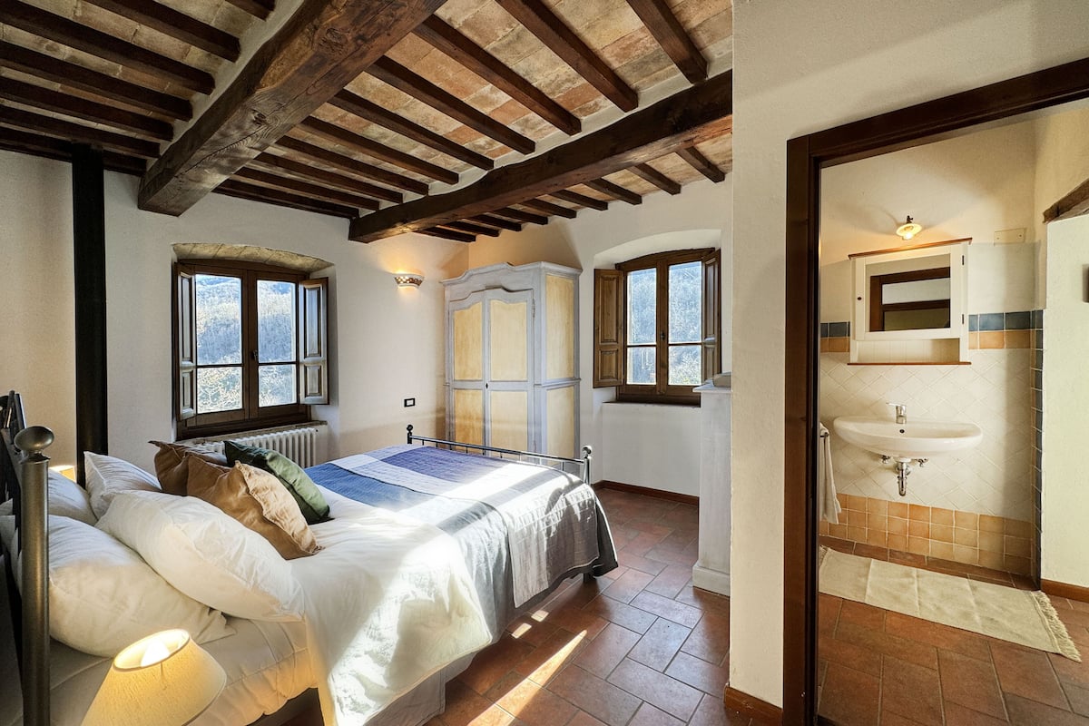 A bedroom with a bed, bedside lamp, and a view of the outside through a window.
