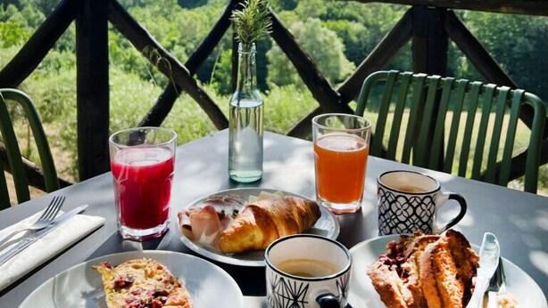 A table set with breakfast items, including croissants, a bottle of water, and a glass of juice, with a scenic mountain view in the background. - Bio Agriturismo il Vigno (Caprese Michelangelo)
