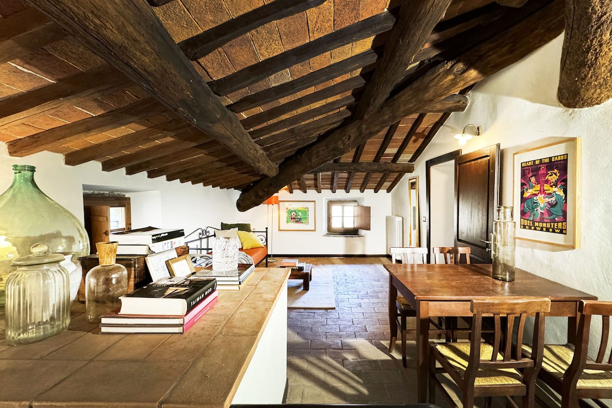 A rustic room with exposed wooden beams, a brick floor, a wooden table, and a framed poster on the wall.