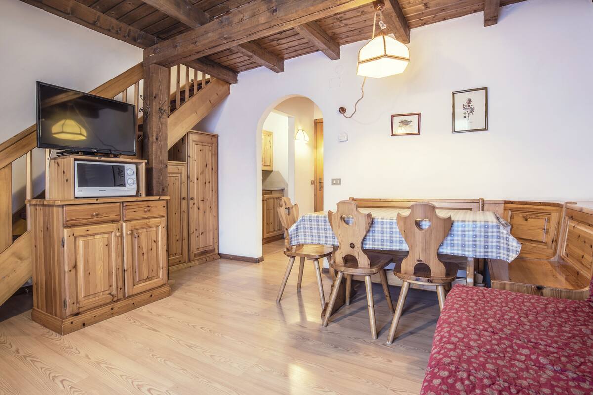 A wooden interior with a dining table, chairs, a television, and a microwave.
