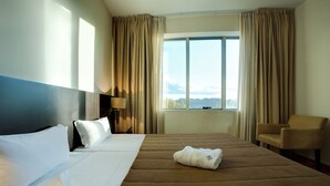 Una habitación de hotel con una cama grande, una silla, una lámpara y vistas al exterior.