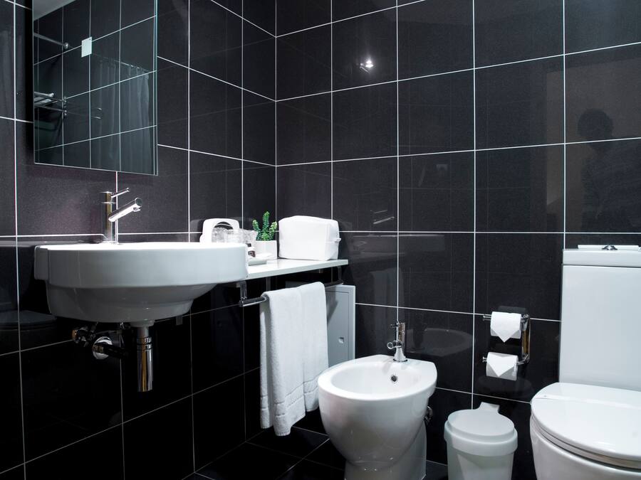 A modern bathroom with a large mirror, a white sink, a bidet, a toilet, and a trash can.