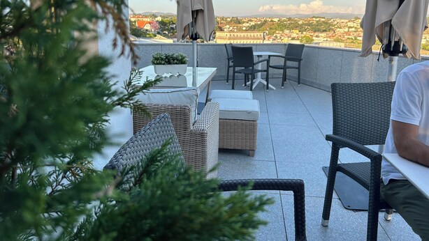 Terraza en la azotea con mobiliario de mimbre, una mesa y sillas, con vistas a un paisaje urbano.