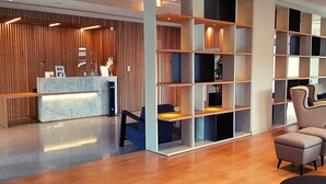 Una moderna zona de recepción con mostrador de mármol, paneles de madera y un área de estar con sofás y pufs.