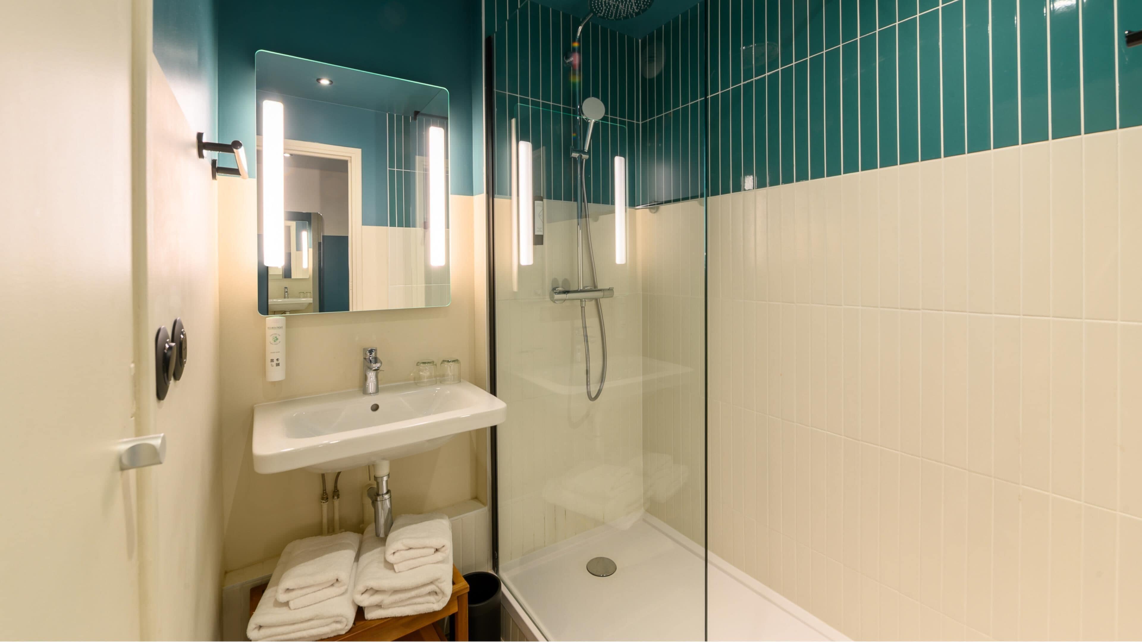 Une salle de bain moderne avec une douche à parois de verre, un lavabo avec un miroir au-dessus et des serviettes soigneusement pliées sur une étagère.