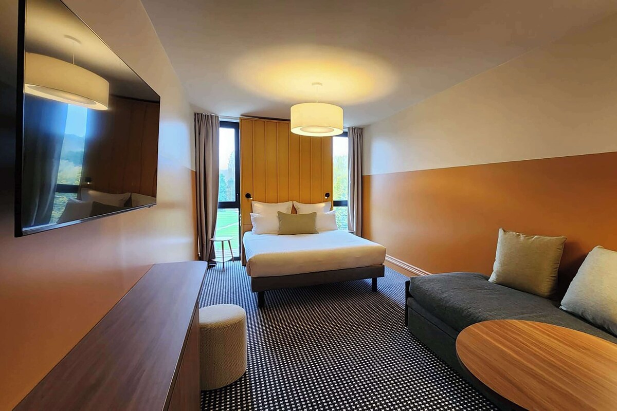 A hotel room with a bed, a sofa, a small table, and a mirror.
