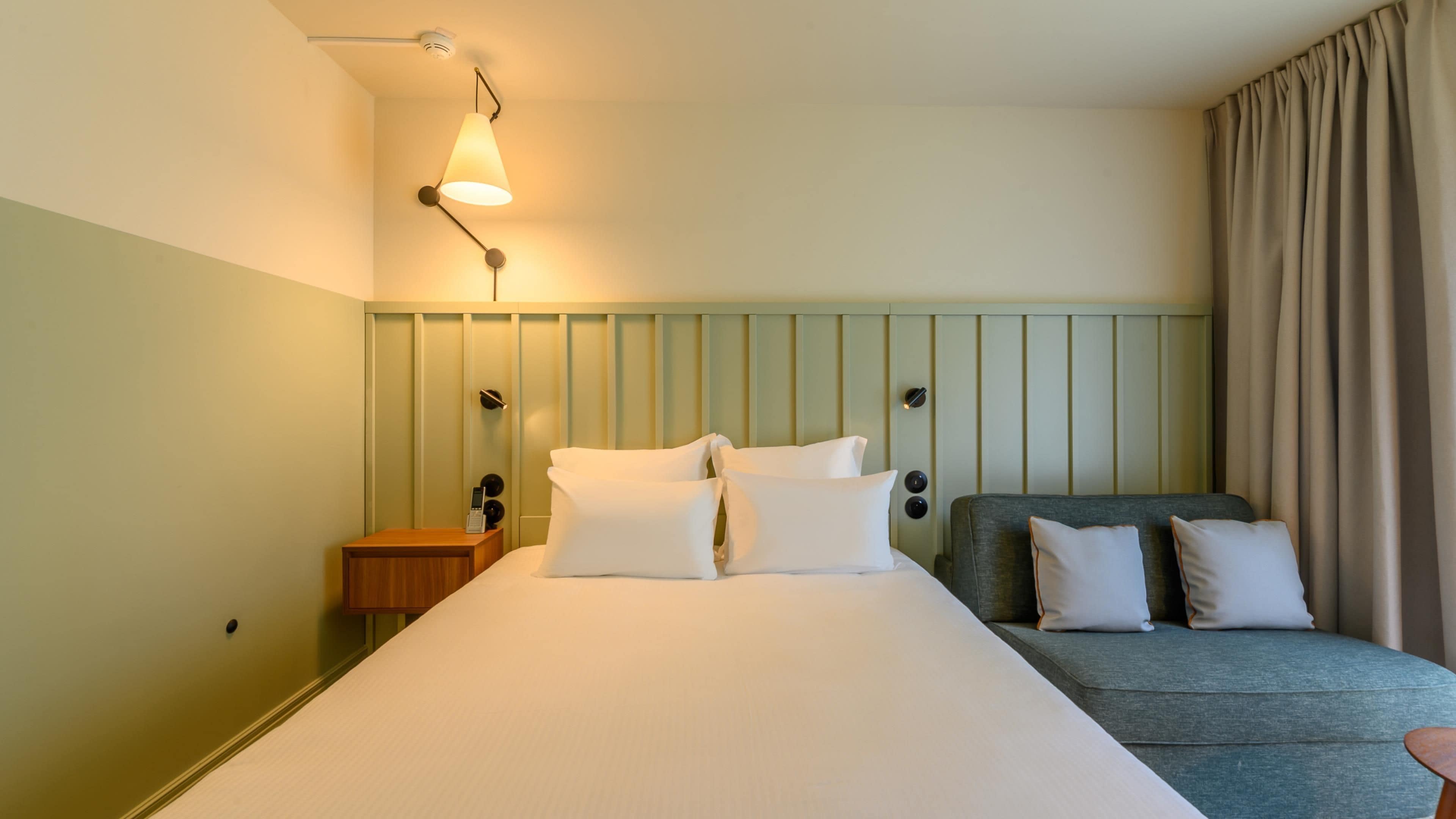 A hotel room with a bed, bedside table, lamp, and curtains.