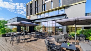 An outdoor seating area with tables and chairs, umbrellas, and a wooden deck. - Kyriad Prestige Compiègne Hotel & Spa (Compiègne)
