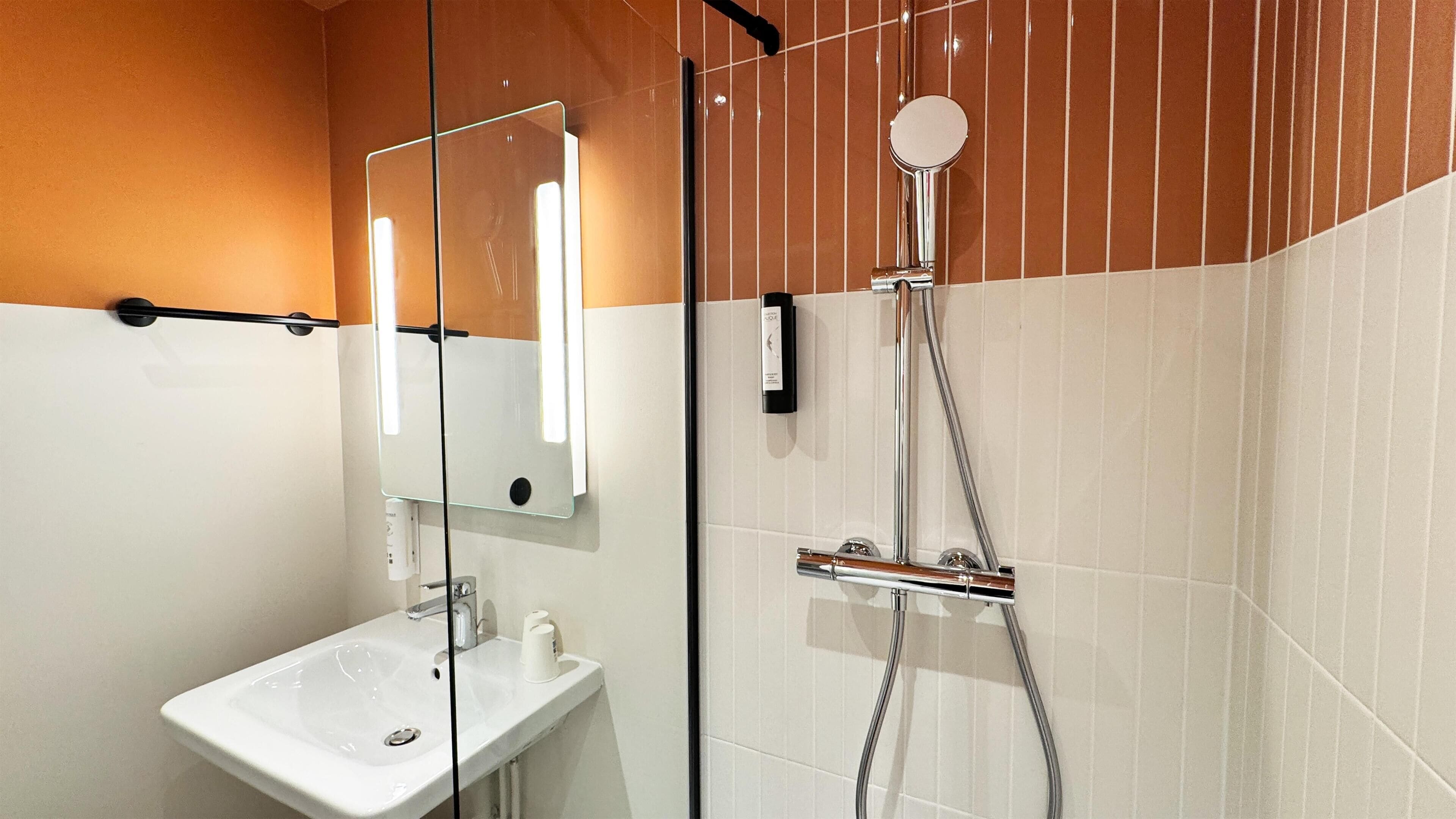 Een moderne badkamer met een douchecabine van glas, een witte wastafel en een spiegel met verticale verlichting.