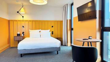 Habitación de hotel con cama, mesita de noche, lámpara, televisión y una pequeña mesa redonda con una silla.