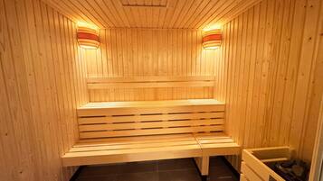 A sauna with wooden walls and benches, equipped with wall-mounted lights.