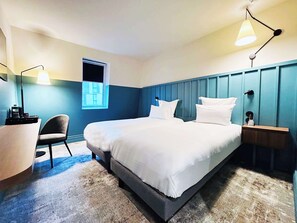 A modern hotel room with a large bed, a desk, a chair, and a window.