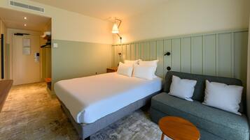 A hotel room with a bed, a sofa, a small table, and a wall-mounted lamp.
