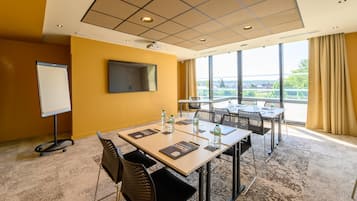 A conference room with a large table, chairs, a whiteboard, and a large window with a view of greenery.
