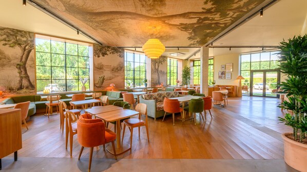 A spacious dining area with wooden tables and chairs, large windows, and a ceiling mural.