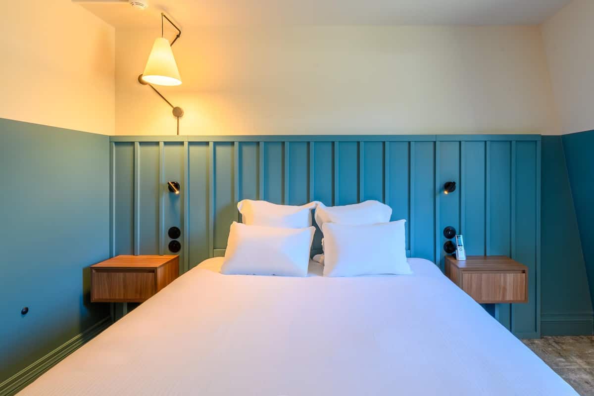 A bedroom with a bed, two bedside tables, a wall-mounted lamp, and a ceiling light.