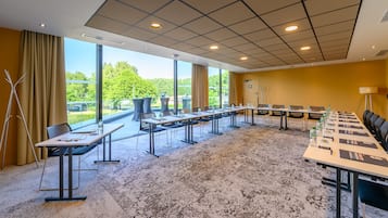 Un salón de conferencias con una larga mesa, sillas y vistas al exterior con vegetación.