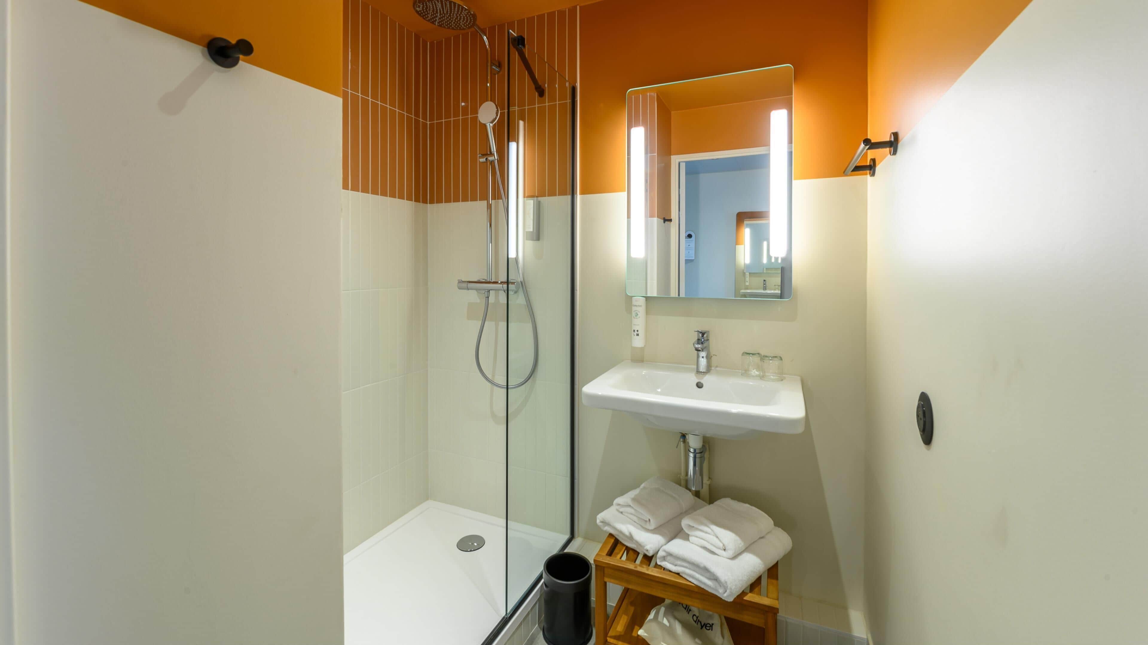 Un baño moderno con ducha de vidrio, lavamanos blanco y un espejo encima.