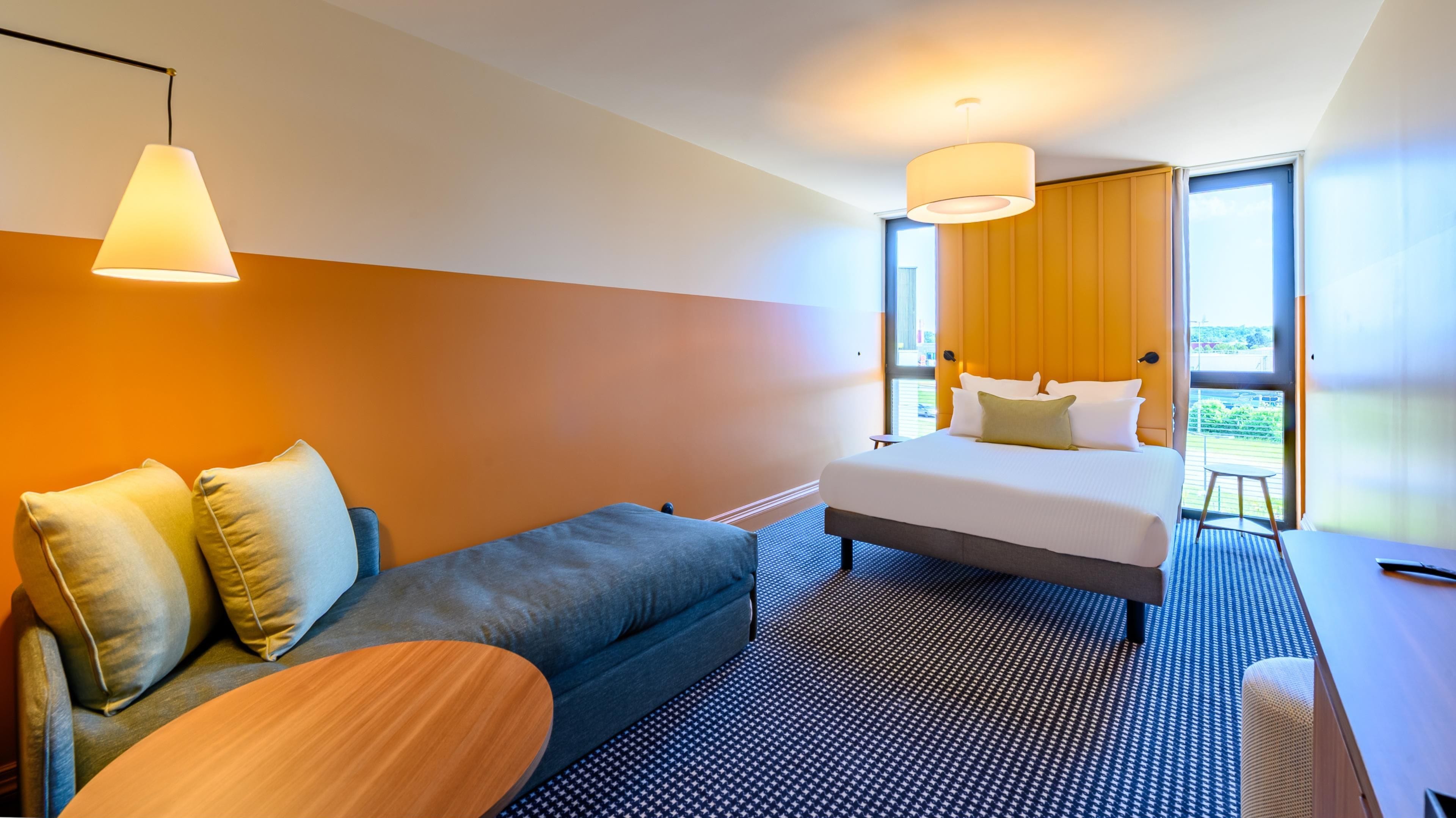 Habitació d'hotel moderna amb llit, sofà, taula petita i finestra gran que ofereix una vista.