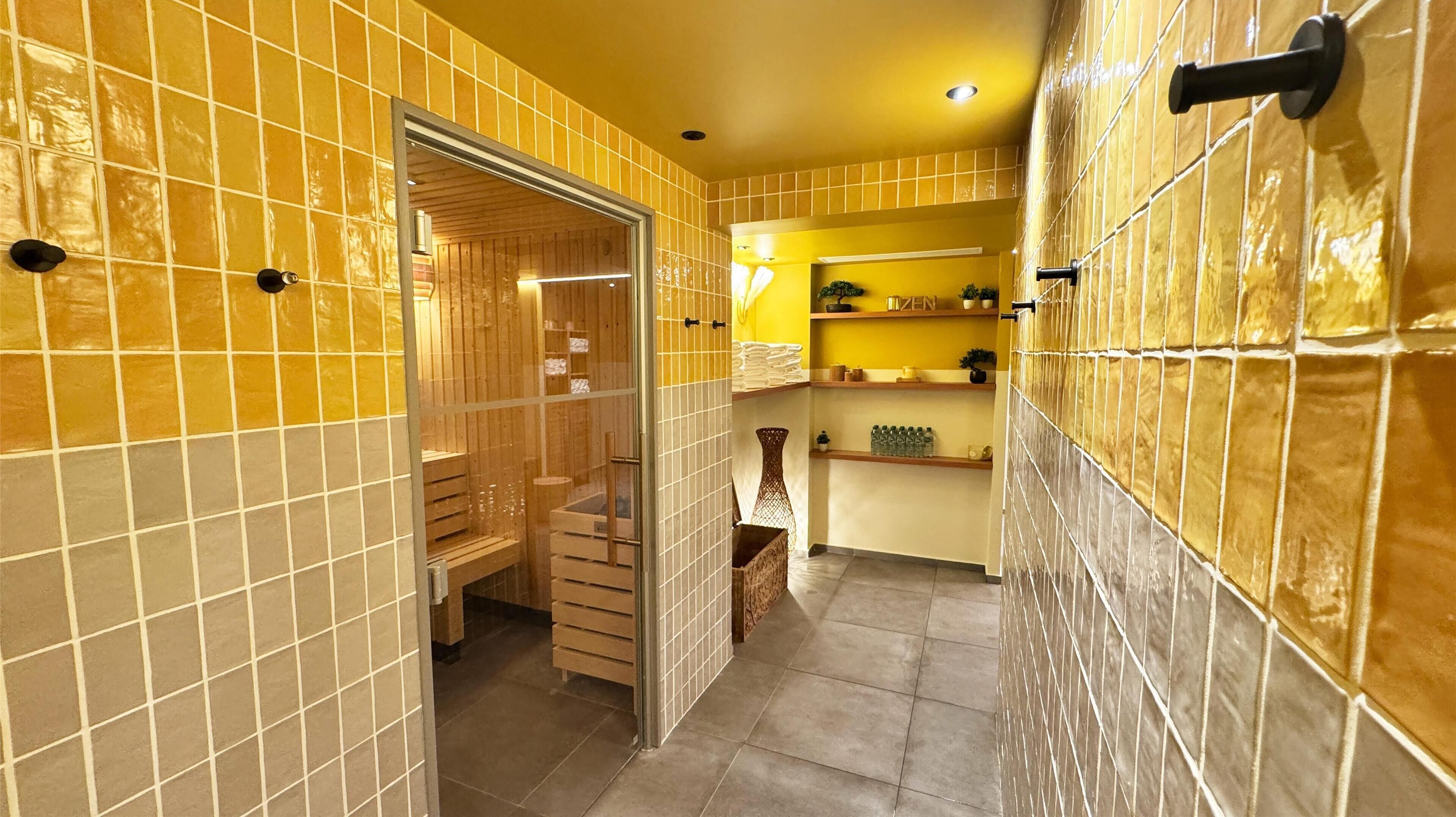 Un baño con paredes de azulejos amarillos, recinto de ducha de madera y una pequeña estantería con artículos de aseo.