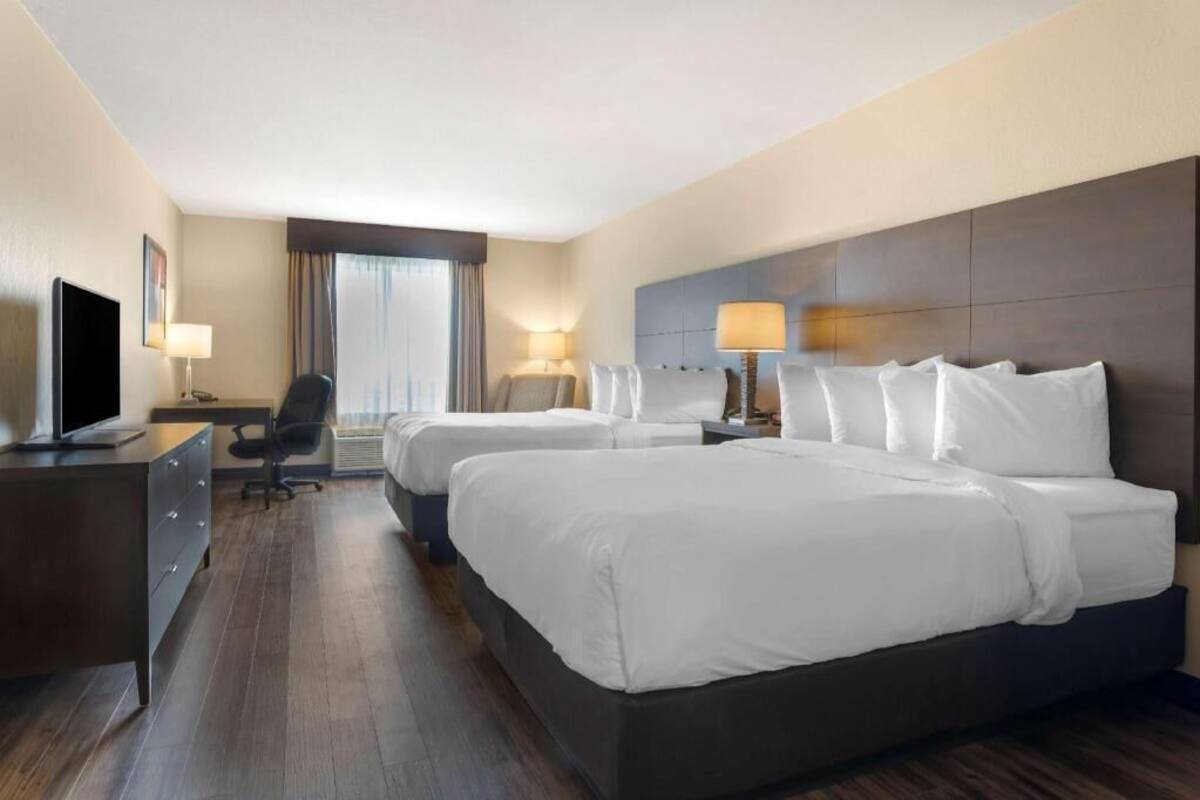 A hotel room with two beds, a desk, a chair, a TV, and a window with curtains.