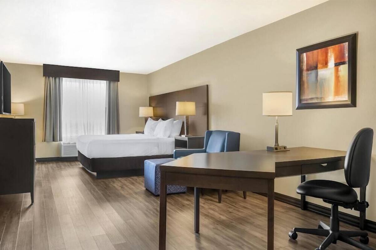 Una habitación de hotel con cama, escritorio, silla y un cuadro en la pared.