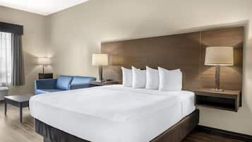 Una habitación de hotel con una cama grande, dos mesitas de noche con lámparas, un sillón azul y una ventana con cortinas.