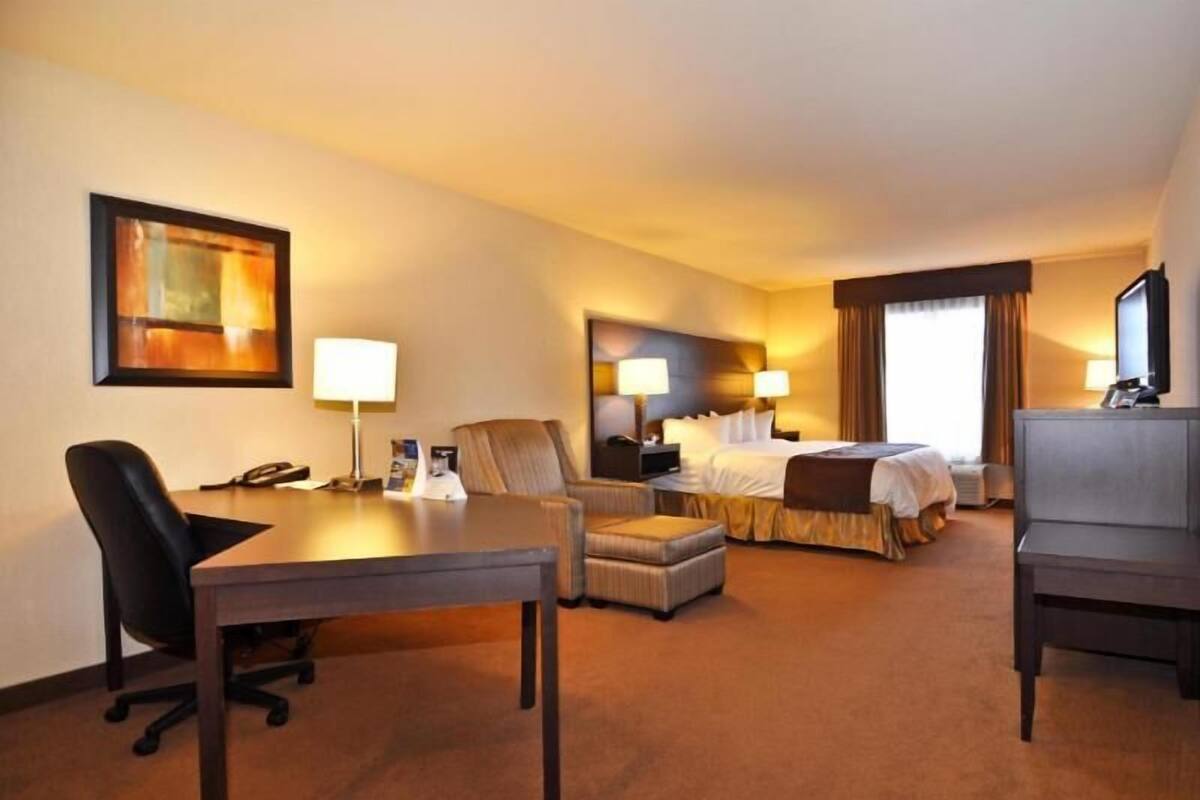 A hotel room with a desk, chair, bed, ottoman, and a television.