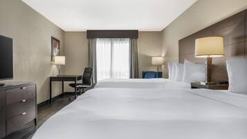 A hotel room with two beds, a desk, a chair, a TV, and two lamps.