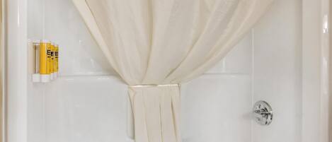 Une salle de bain avec un rideau de douche attaché en haut, une barre d’appui et un ensemble de bouteilles jaunes et blanches fixées au mur.