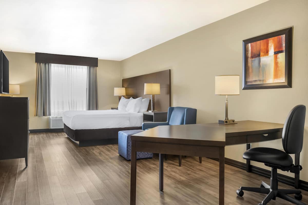 A hotel room with a bed, desk, chair, and artwork on the wall.
