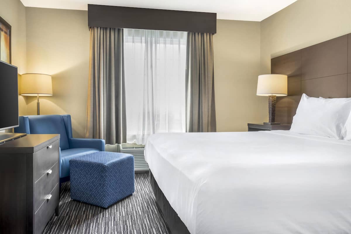 A hotel room with a large bed, a chair, a desk, and a TV.