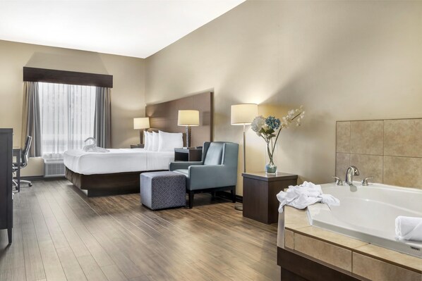 Habitación de hotel con una cama grande, un escritorio, una silla, tocador con bañera y ventana con cortinas.