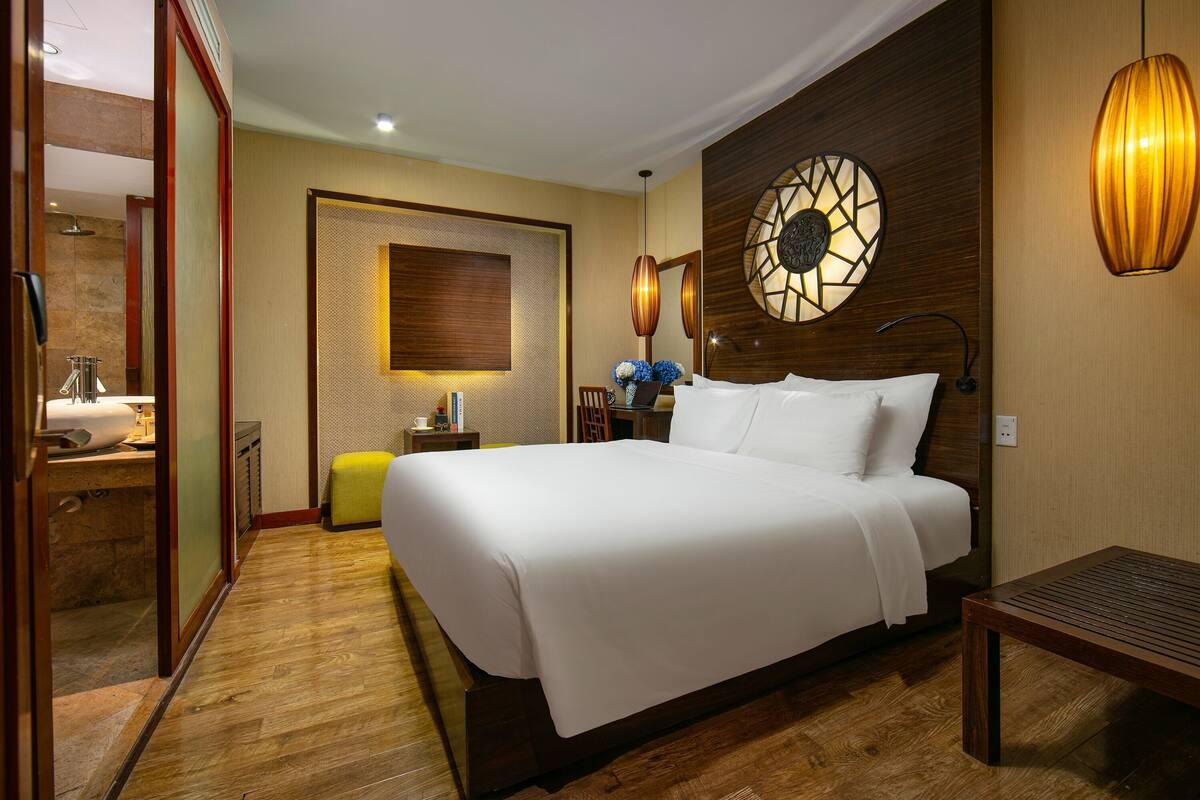 Une chambre d’hôtel avec un grand lit, un plancher en bois, une lampe fixée au mur et une petite table.