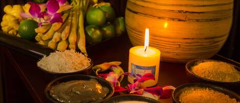 A table with various items including a lit candle, bowls of different substances, and a bowl of fruits and flowers.
