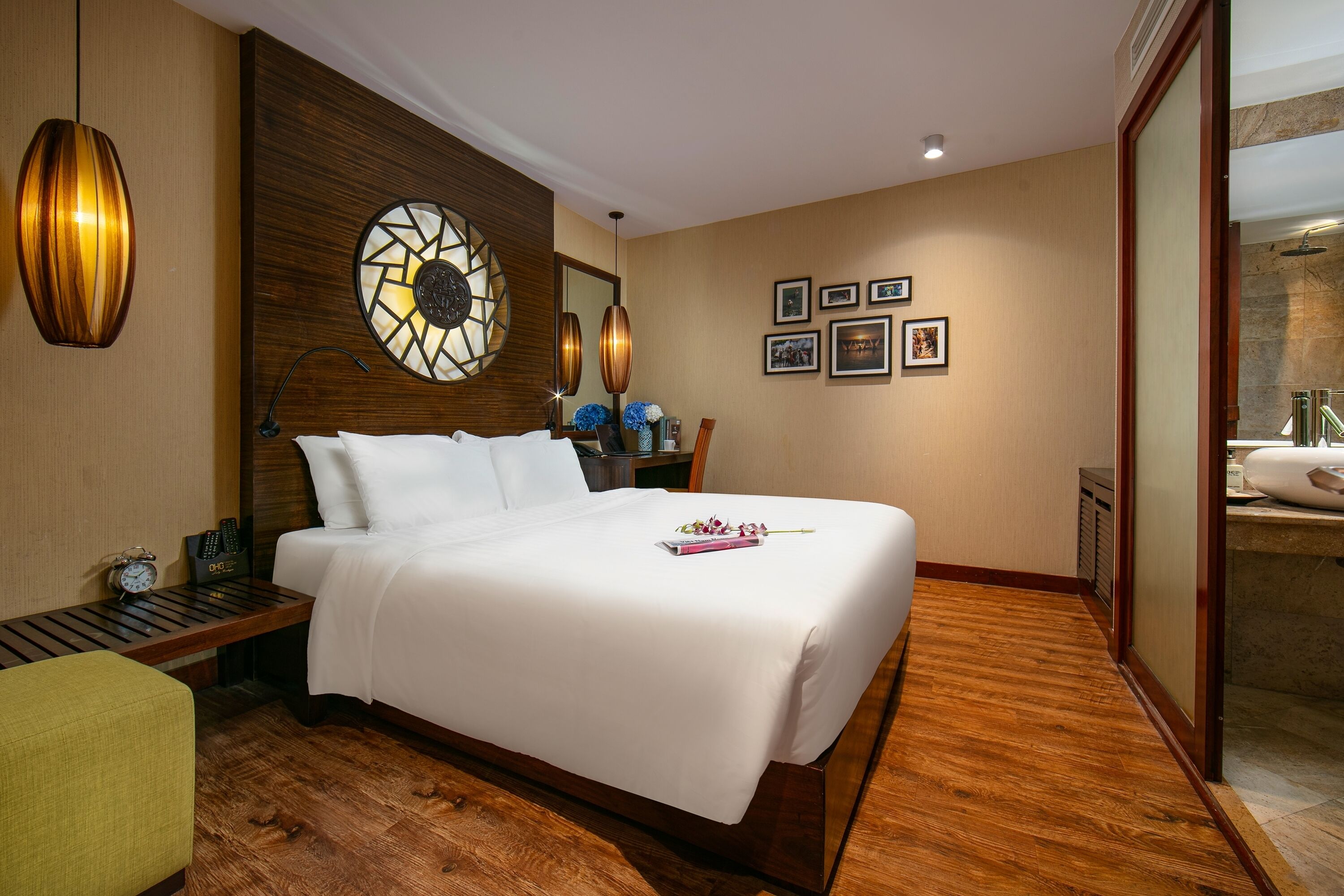 A hotel room with a large bed, wooden flooring, a wall clock, and a mirror.
