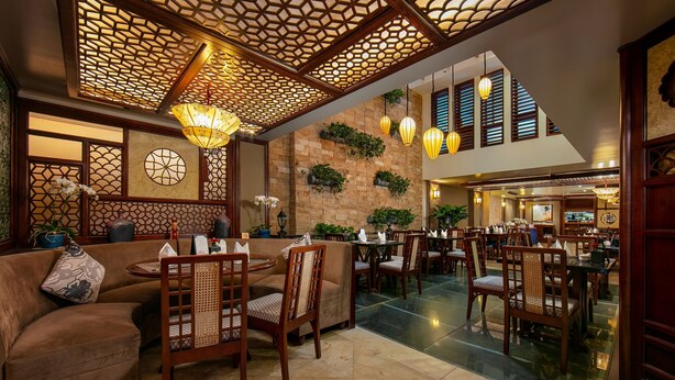 Un hall d’entrée spacieux avec un plafond haut, un décor de treillis en bois et de nombreux espaces de détente, notamment des canapés et des tables.