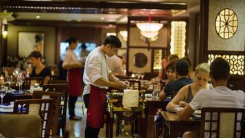 A restaurant interior with wooden furniture, tables, and a waiter serving guests.