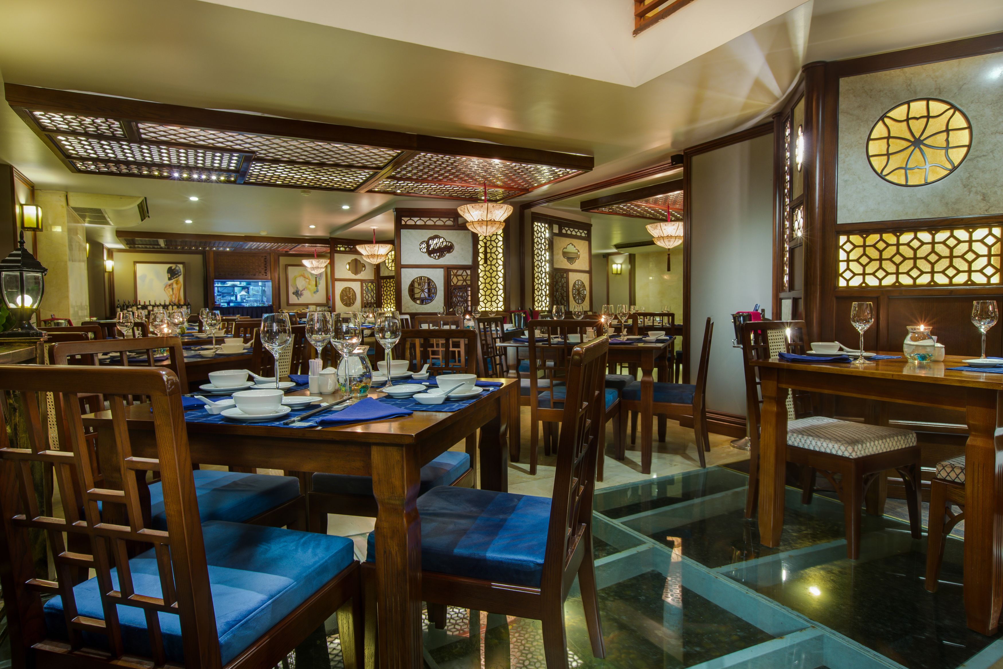 A restaurant with wooden tables and blue cushioned chairs, a television screen, and decorative wall panels.
