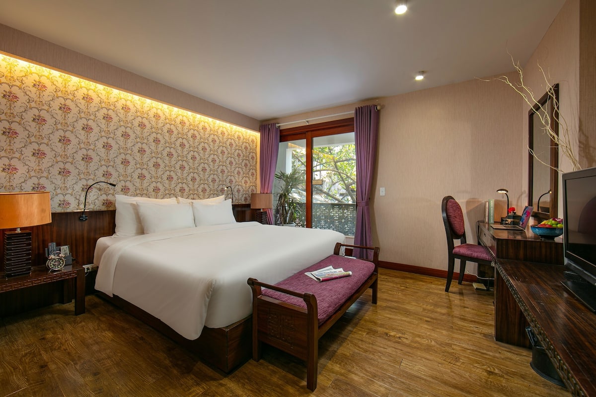 Une chambre d’hôtel avec un grand lit, un bureau avec une chaise, une télévision et une fenêtre avec des rideaux.