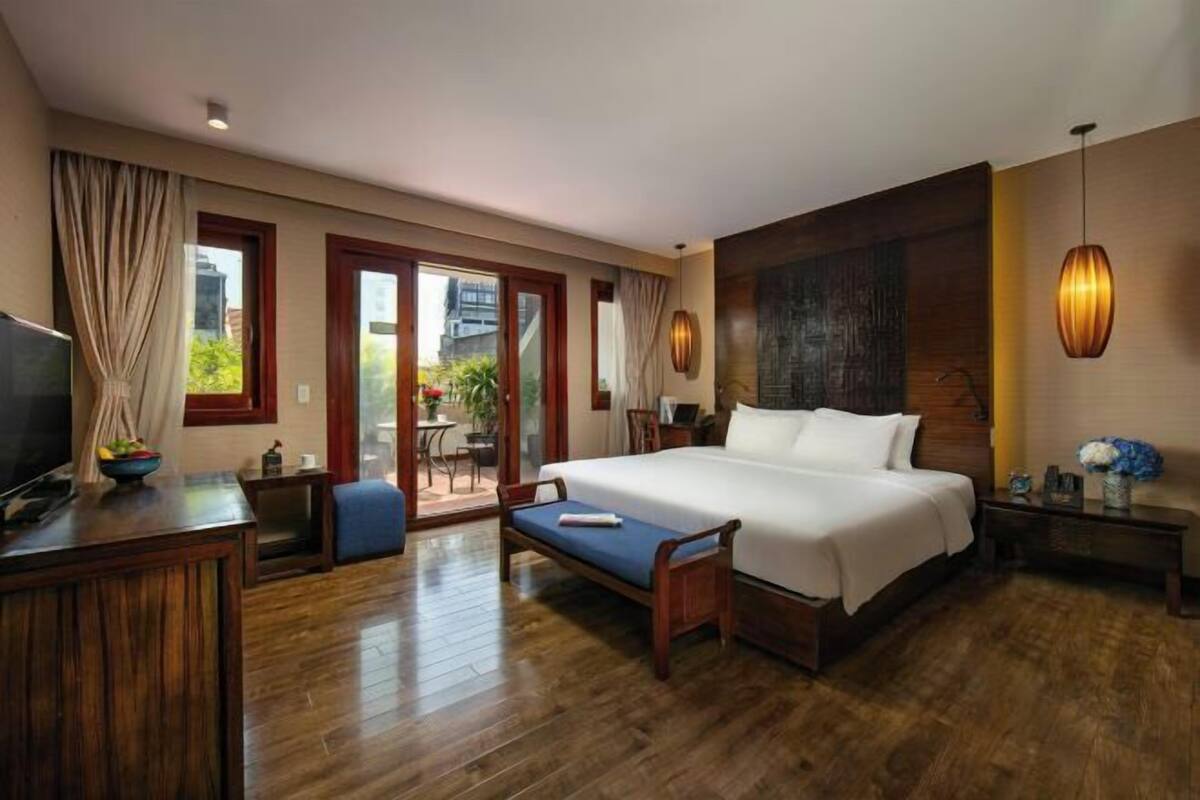 Une chambre d’hôtel dotée d’un grand lit, d’un plancher en bois, d’un bureau avec une télévision et d’un balcon aménagé avec du mobilier d’extérieur.