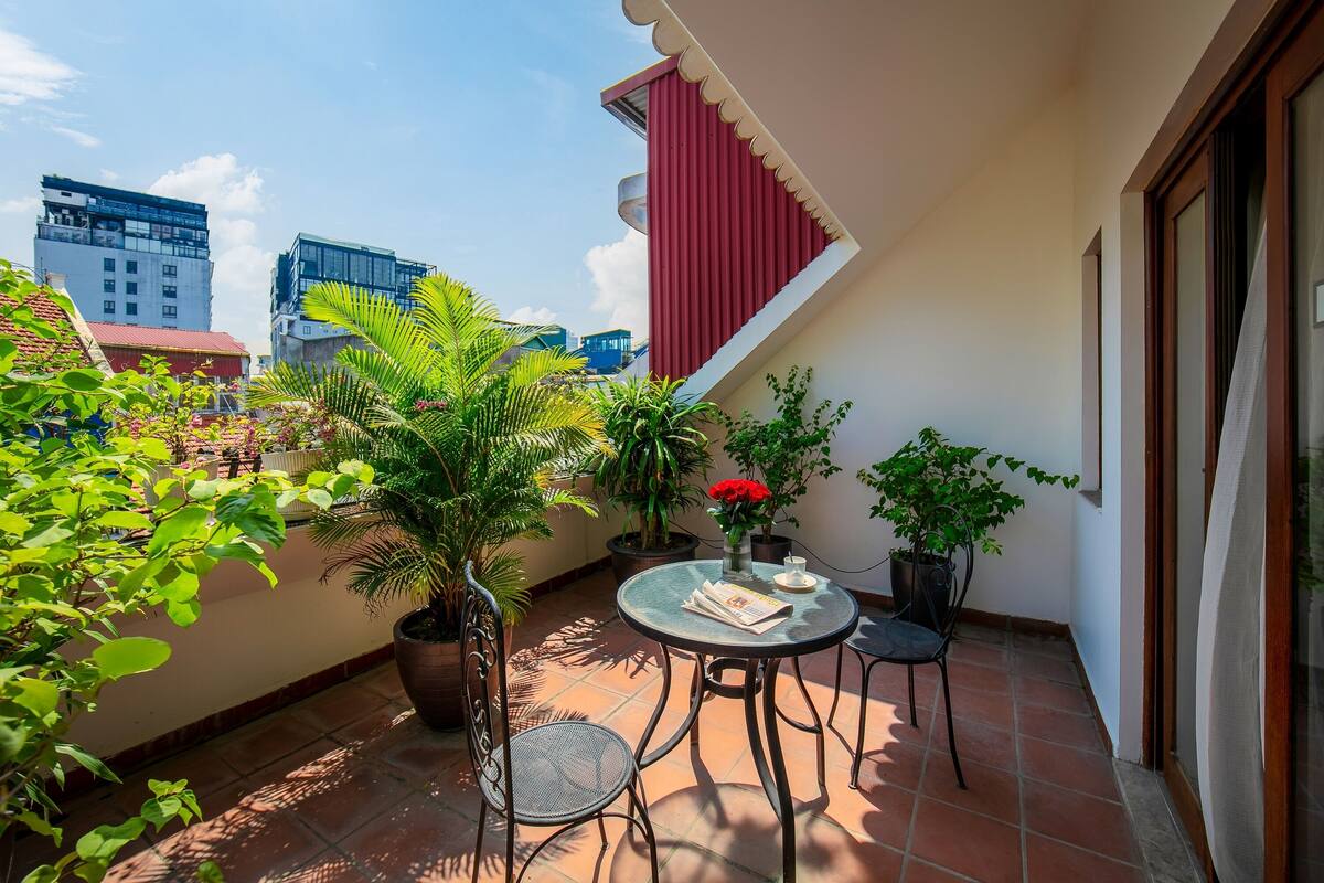 Un balcon agrémenté de plantes en pot, une table avec une chaise et un auvent rouge.