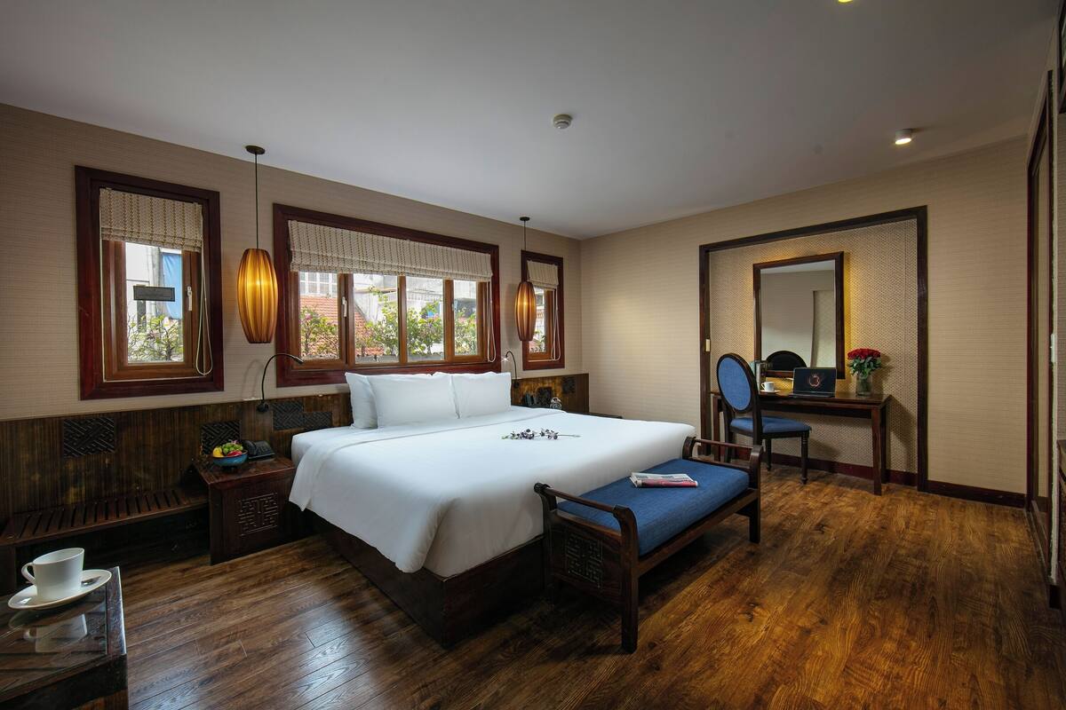 Une chambre d’hôtel avec un grand lit, un plancher en bois, un bureau avec un ordinateur portable, une chaise et une petite table avec une tasse.