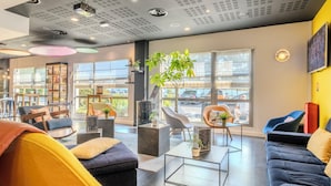 A modern living room with a sofa, chairs, a coffee table, and a bookshelf. - Campanile Roissy - Aéroport CDG - Le Mesnil Amelot (Le Mesnil-Amelot)