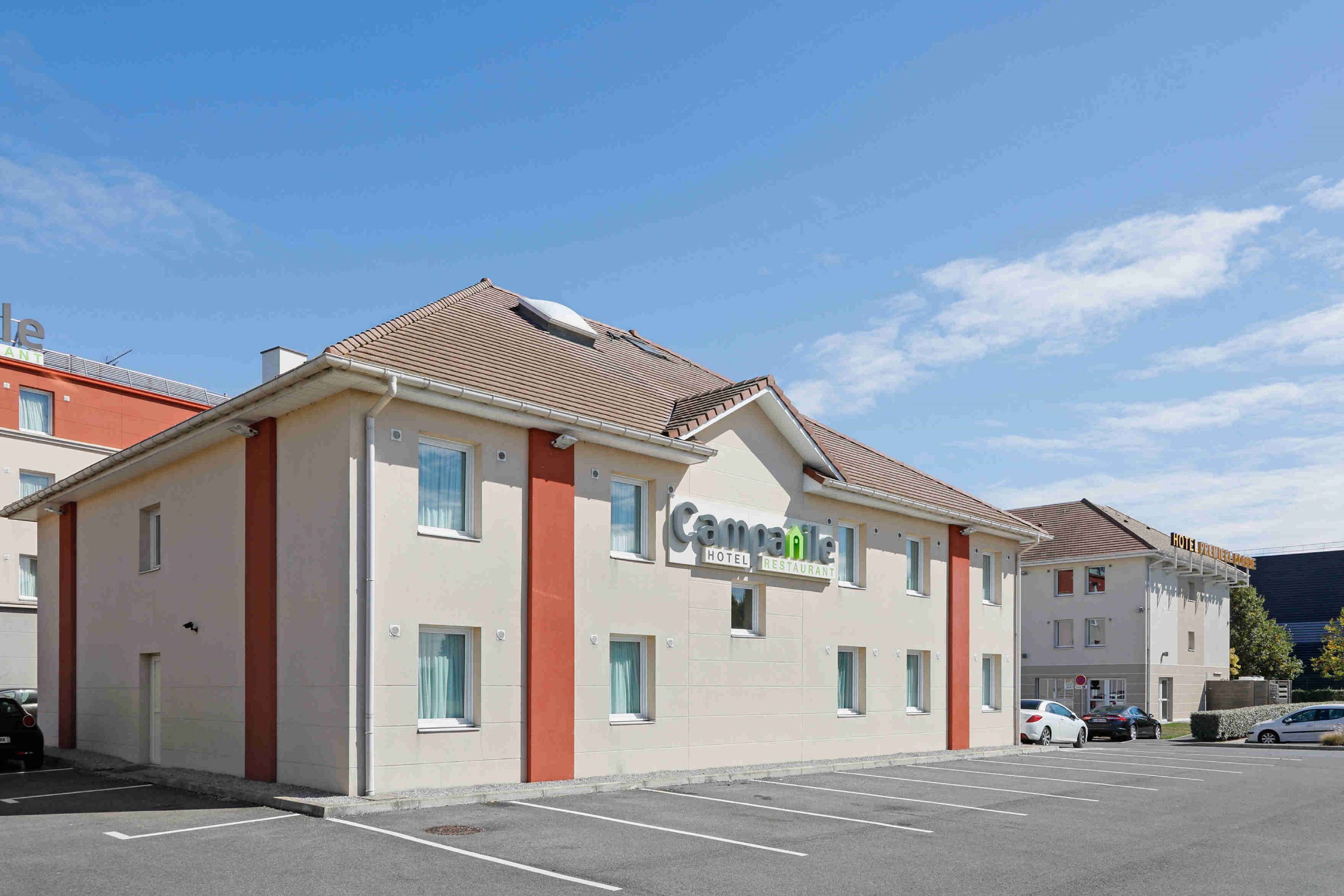 Ett hotell med en enkel fasad, en skylt med texten ”Campanile Hotel Restaurant” och en parkeringsplats med flera bilar.