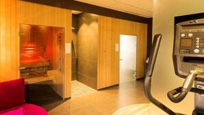 A sauna room with a glass door, a massage chair, and a fitness machine. - Campanile Roissy - Aéroport CDG - Le Mesnil Amelot (Le Mesnil-Amelot)
